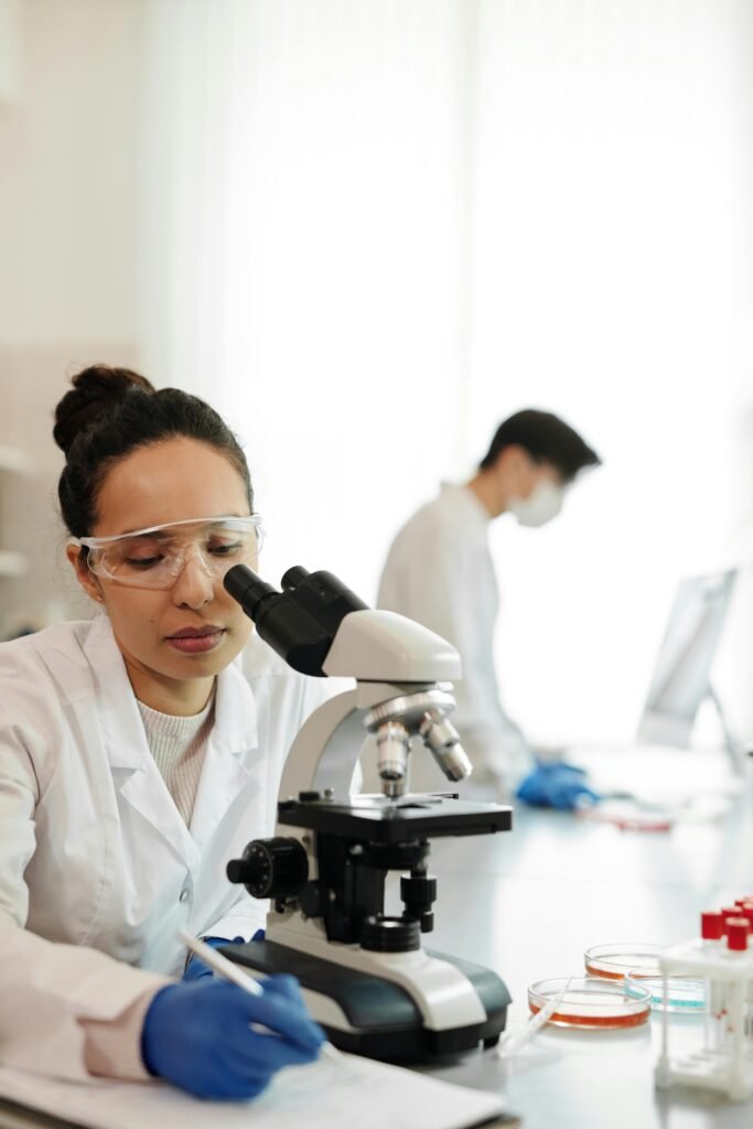 Woman working with microscope in a laboratory, taking notes. Ideal for science and research themes.